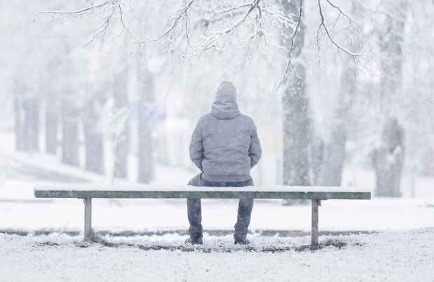 在冬天的暴风雨中，身影坐在长凳上